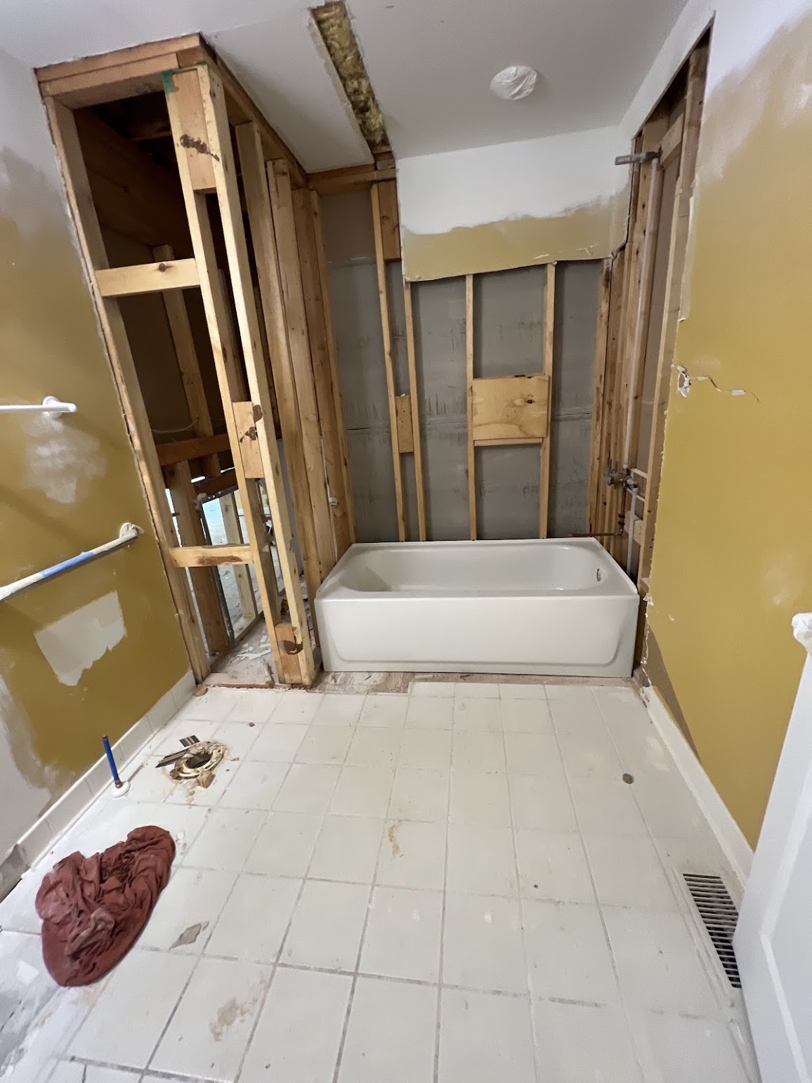 Bathroom during renovation with the tub in place, wall framing exposed, and floor work in progress