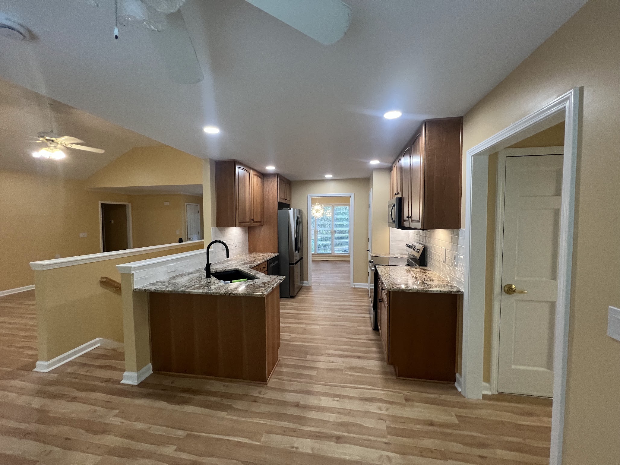 Completed kitchen from another angle, with a sink peninsula, stone countertops, tile backsplash, and updated appliances