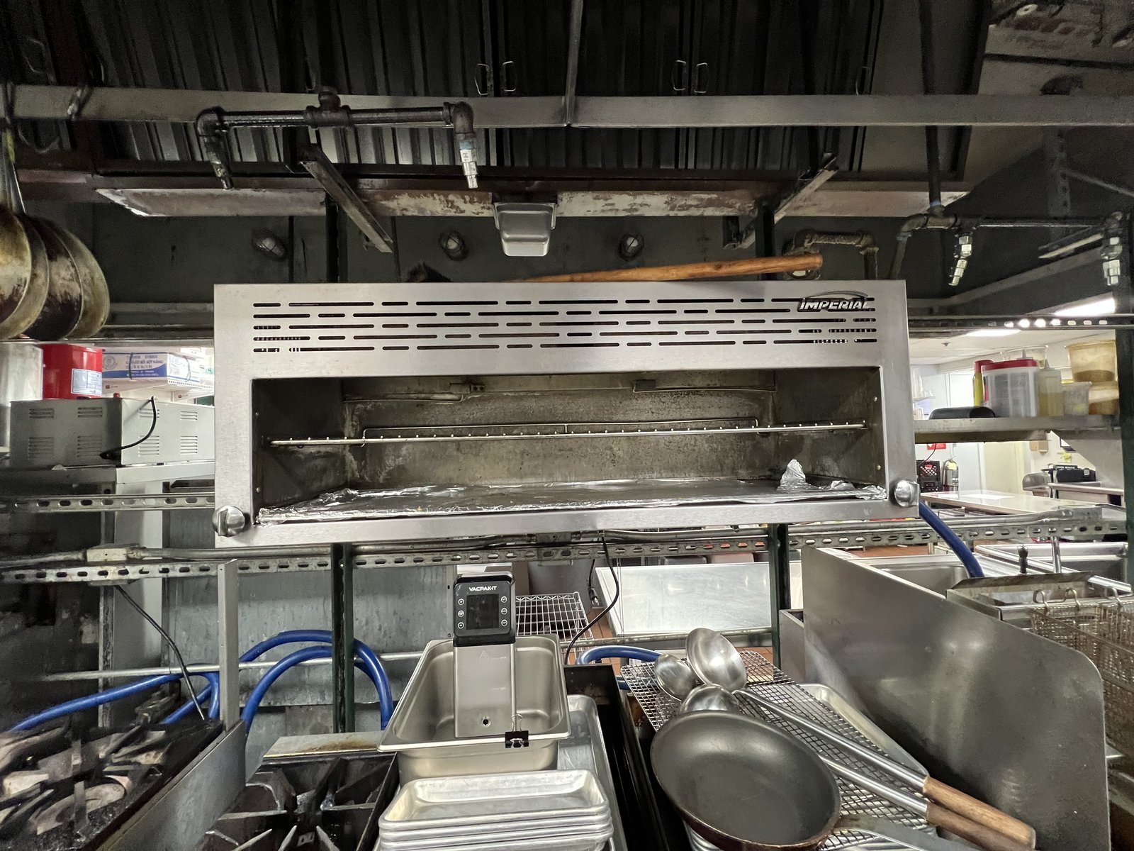 Restaurant cooking line with an overhead broiler, gas burners and fryer baskets visible on the right.